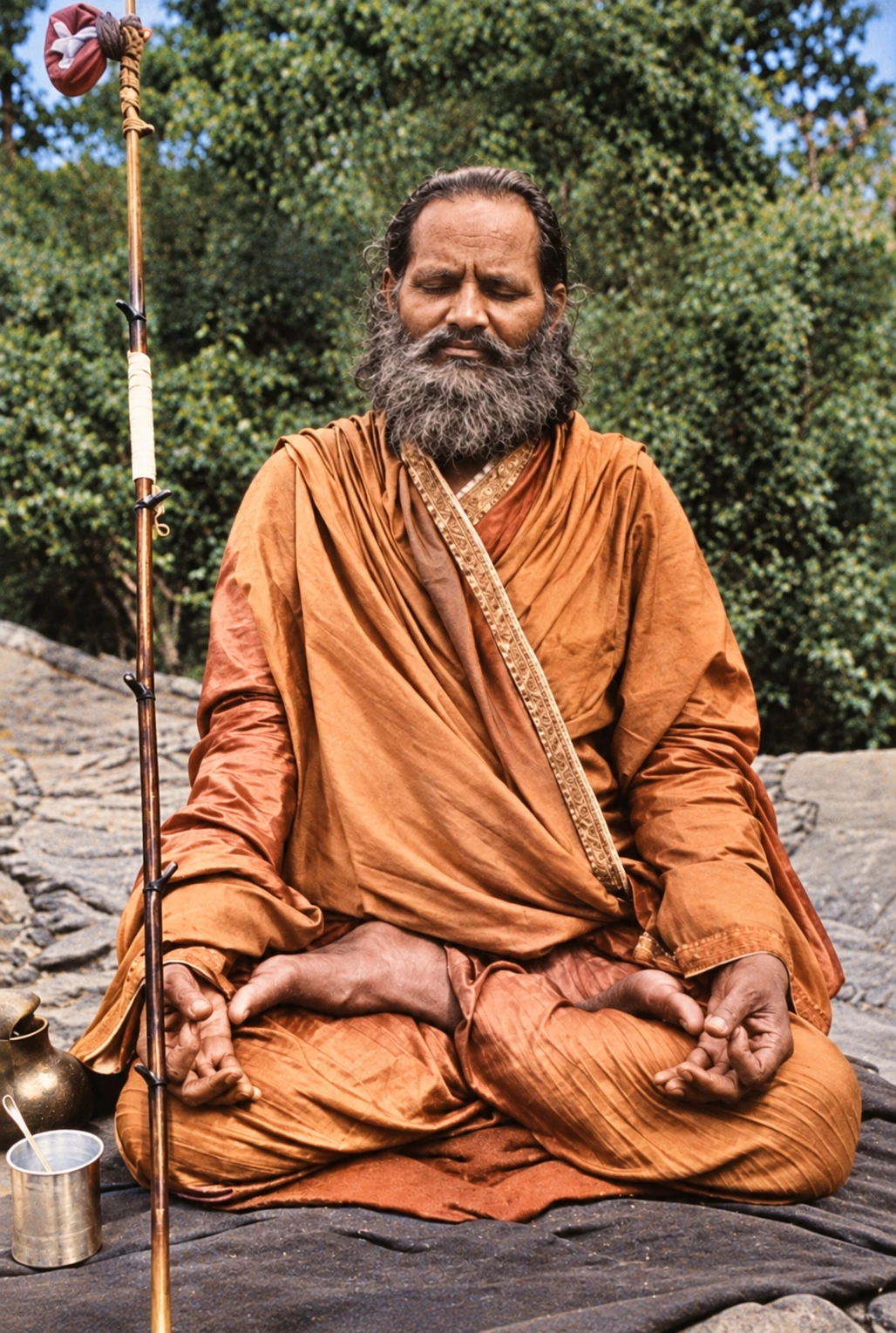 Brahmananda Saraswati meditating cross-legged outdoors beside his staff and a brass water pot