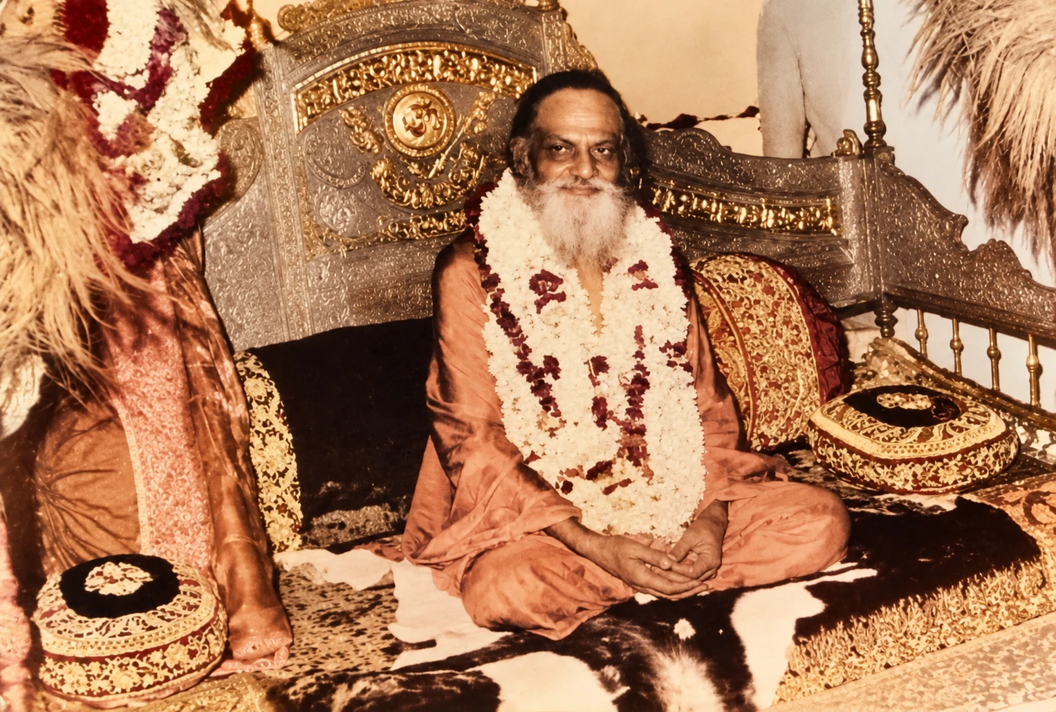 Brahmananda Saraswati smiling, garlanded with flowers, seated cross-legged on a silver throne